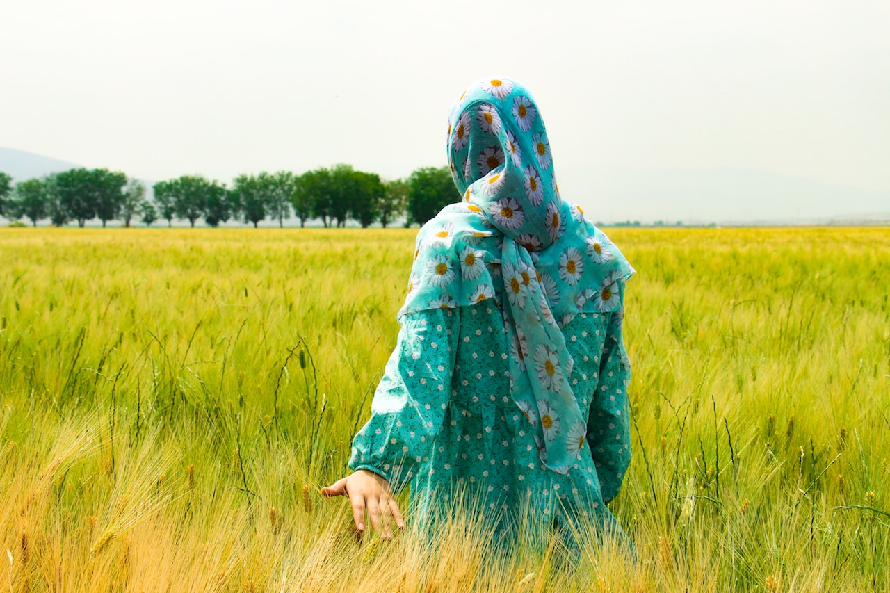 Woman walking through a field trailing her hand in the grass.