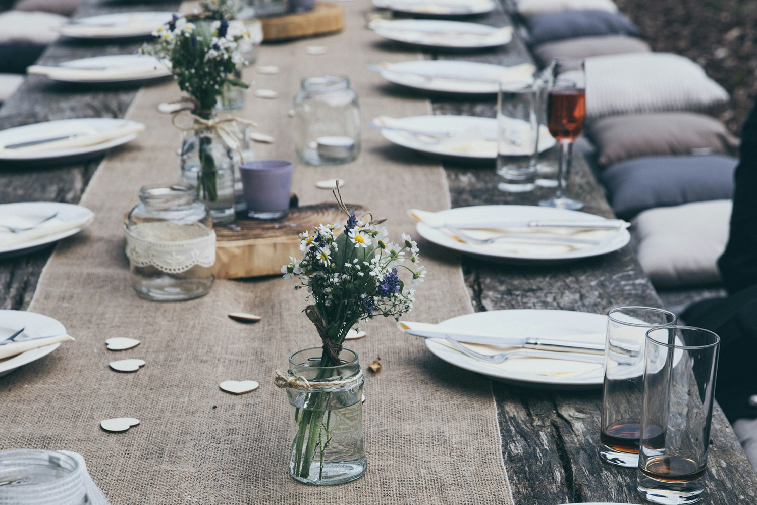 Table setting with white plates and small vases of flowers on a low wooden table outdoors