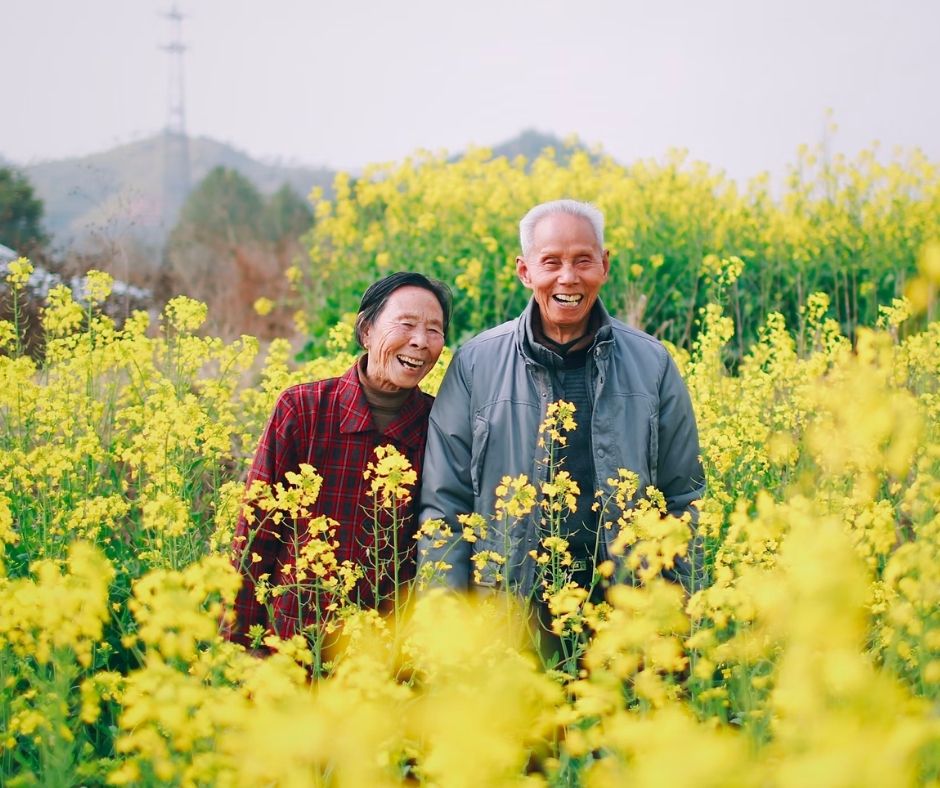 two older people smiling in a field of yellow flowers